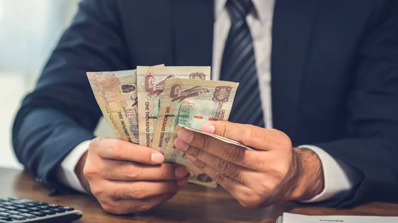 A man counting UAE Dirham banknotes, and calculating the total value with a calculator before signing an agreement.